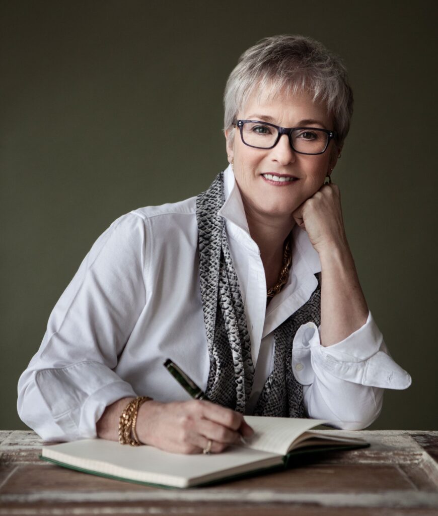 Headshot of Brenda. She is seated at a desk, writing with a pen in a notebook