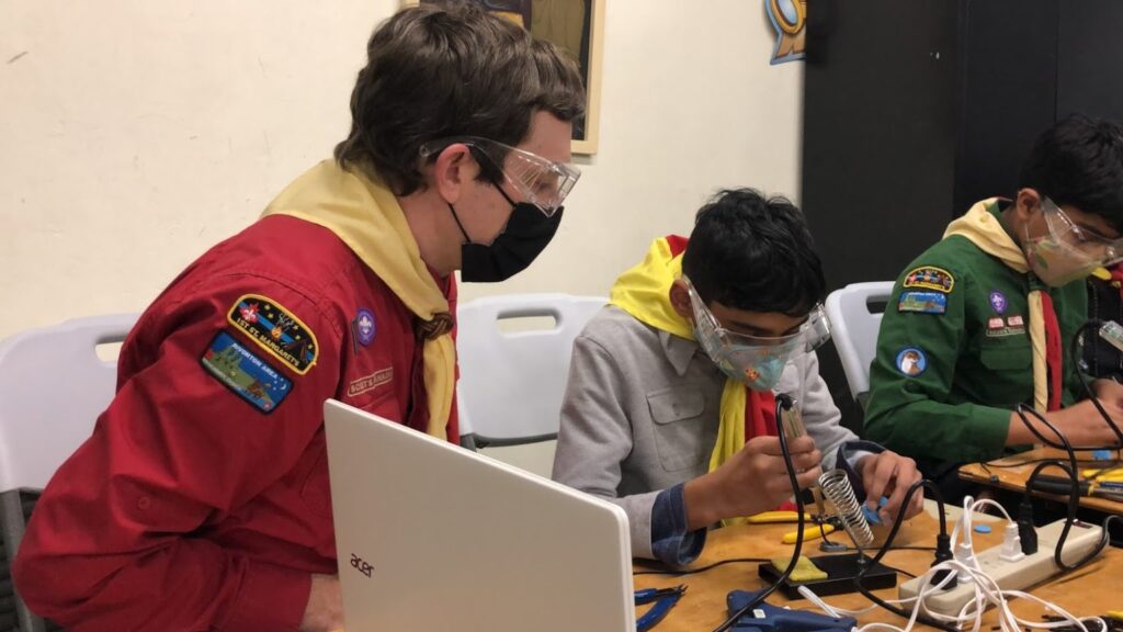 A scout leader watches on as scouts assemble their devices.