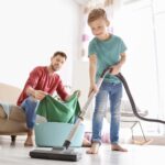 a father does laundry while his son vaccuums