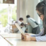 a girl with glasses reads something on a tablet in a classroom