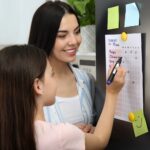 a mother watches as a little girl writes on a to-do list 