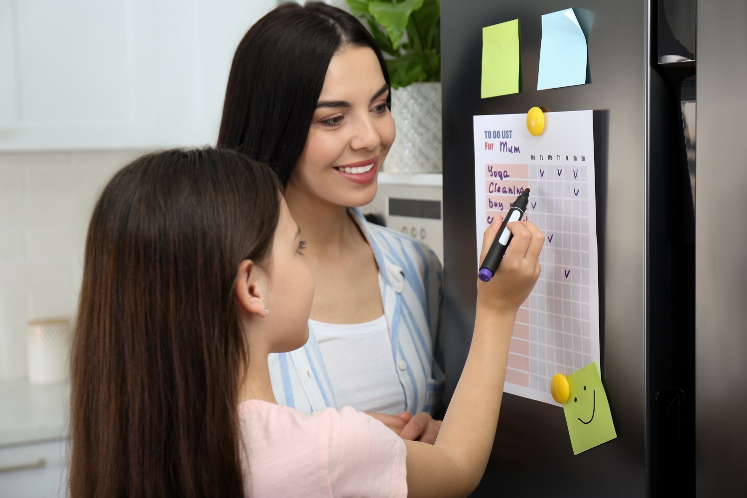 a mother watches as a little girl writes on a to-do list "for mum"