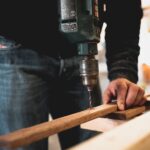man holding a wooden stick while drilling a hole in it