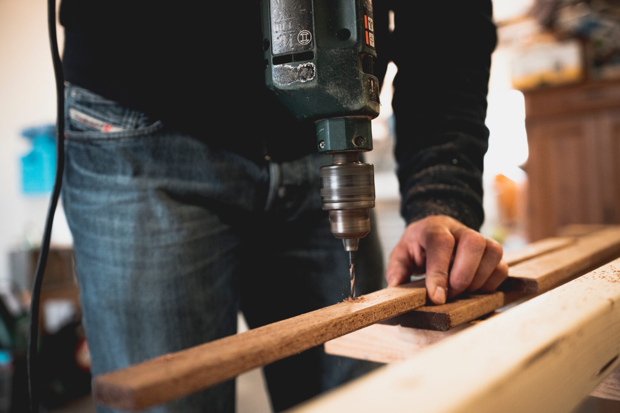 man holding a wooden stick while drilling a hole in it