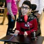 Milad in a wheelchair using a LipSync and a switch to play a video game at an event