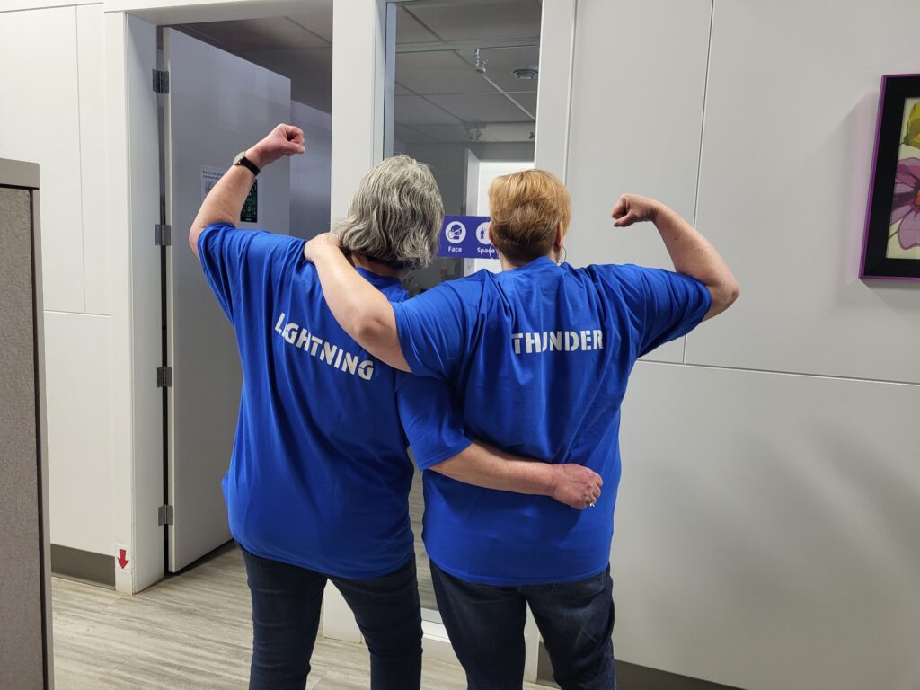 Two Prairie Region employees showing the back of their shirts that say "Lightning" and "Thunder"