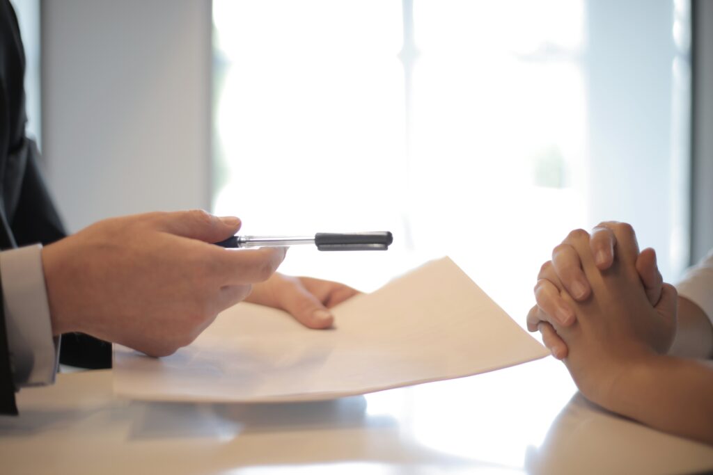a person in a suit handing a customer a paper and pen to sign a document