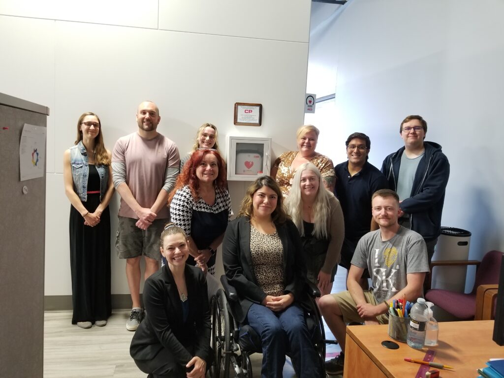 Neil Squire staff in Regina in a group photo with the AED and the plaque thanking CP