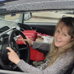 WorkBC Assistive Technology Services participant Robyn holding the steering wheel in her car with a delivery in her passenger seat.