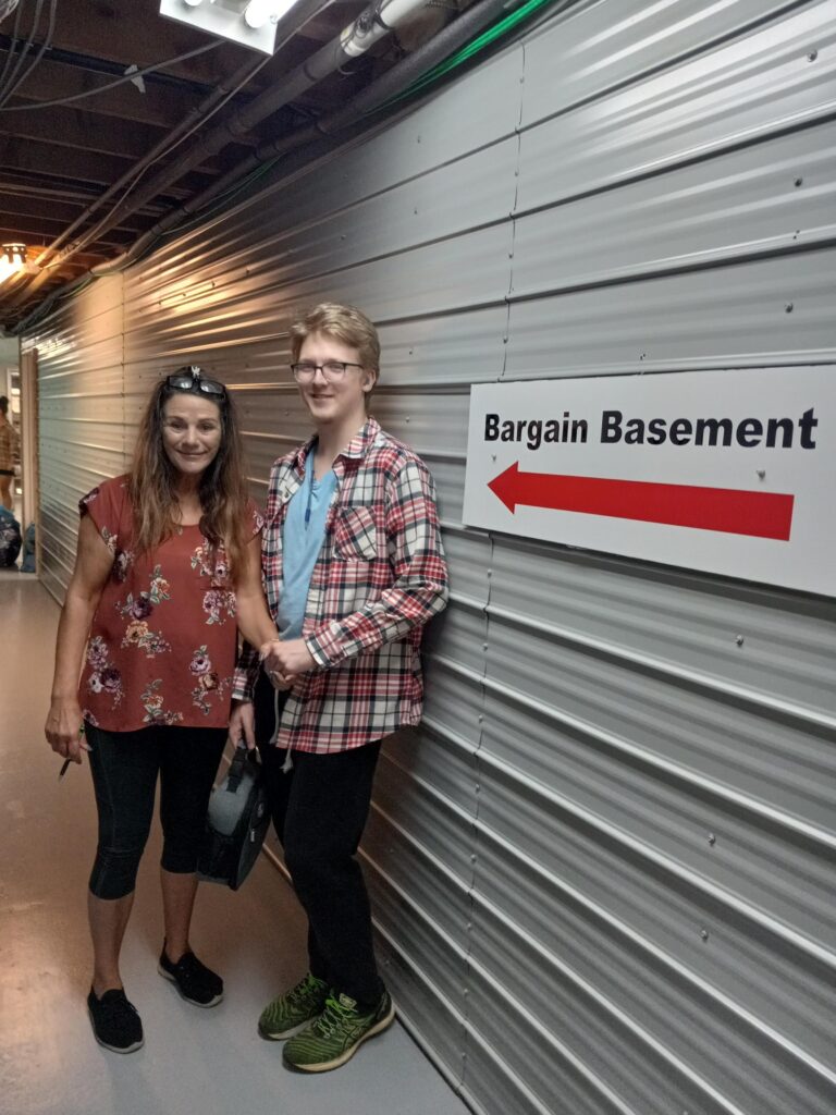 Working Together participant Jacob and his supervisor Bessie in front of a sign for the Bargain Basement
