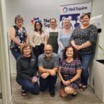 Neil Squire Regional Managers and Case Managers standing together in front of Neil Squire signs