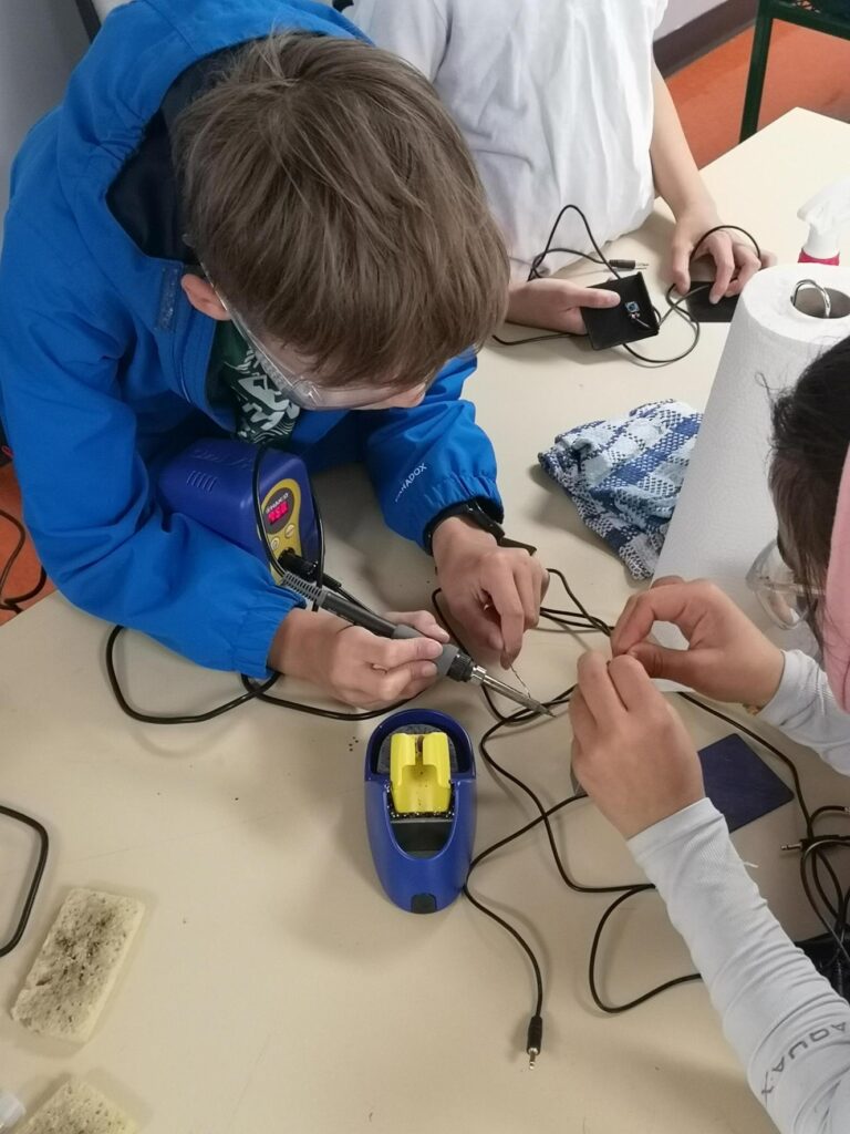 kids making devices together, with one kid holding a soldering gun