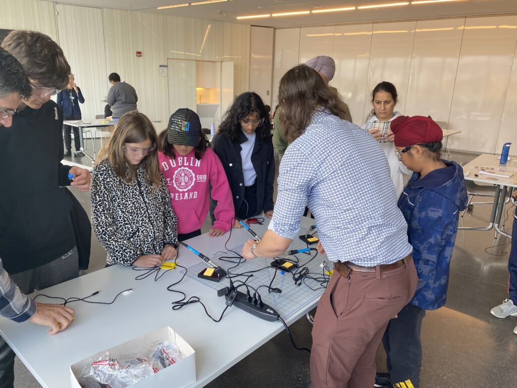 young makers gather around a table at a build event to watch an instructor