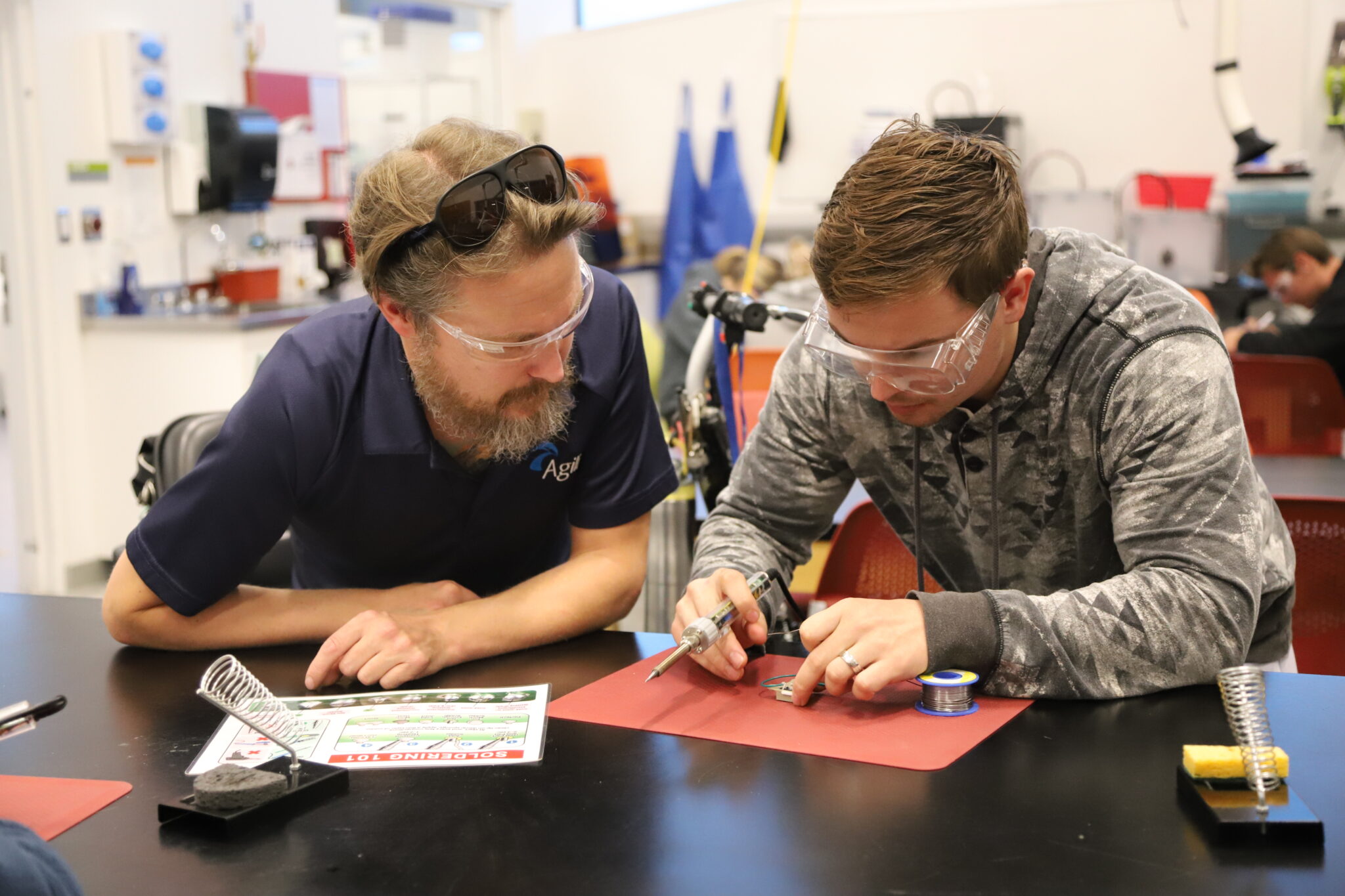 an instructor watches as a student solders