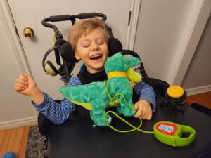 Chester smiles as he plays with a switch adapted dinosaur toy on his wheelchair tray