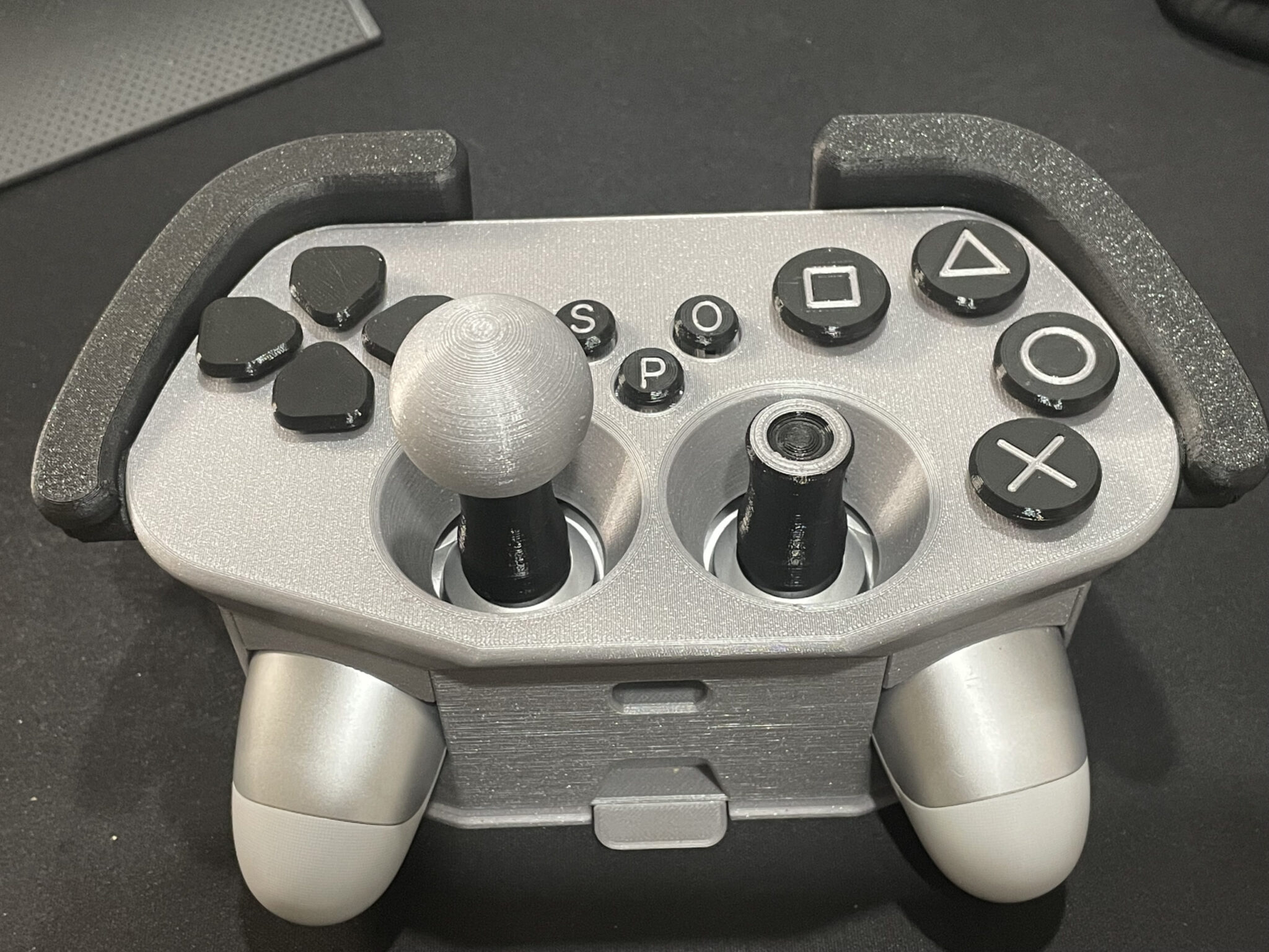 A PS4 controller in a grey and black 3D printed adaptive case, making the buttons larger and more spread out.