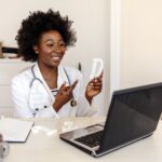 A speech therapist holds a letter in their hands while they conduct an online lesson with a laptop webcam.