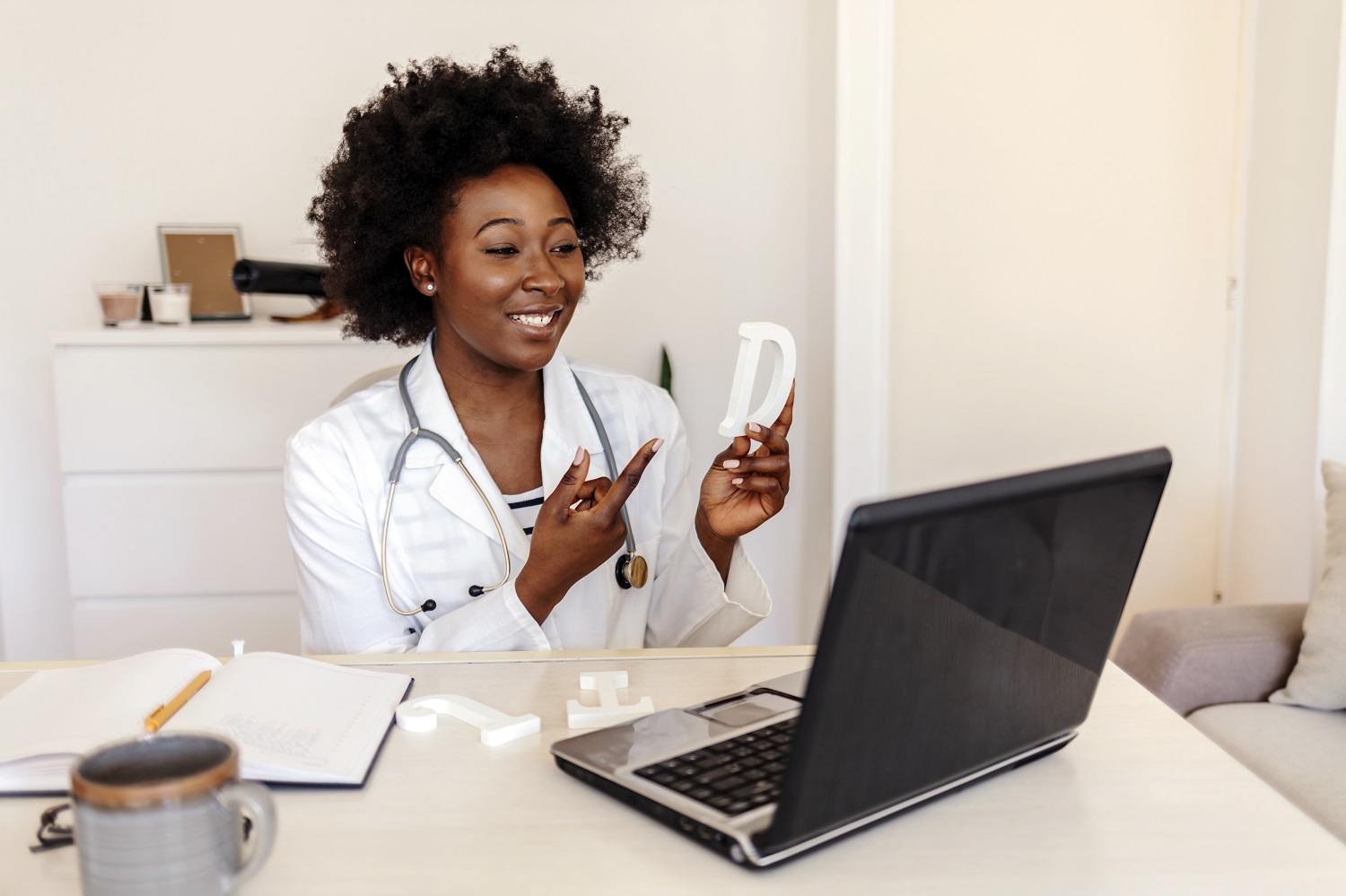 A speech therapist holds a letter in their hands while they conduct an online lesson with a laptop webcam.