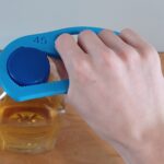 A hand using a Bottle Opener to open a bottle of apple juice.