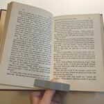 Person using book holder device to hold open pages of a book with one hand.