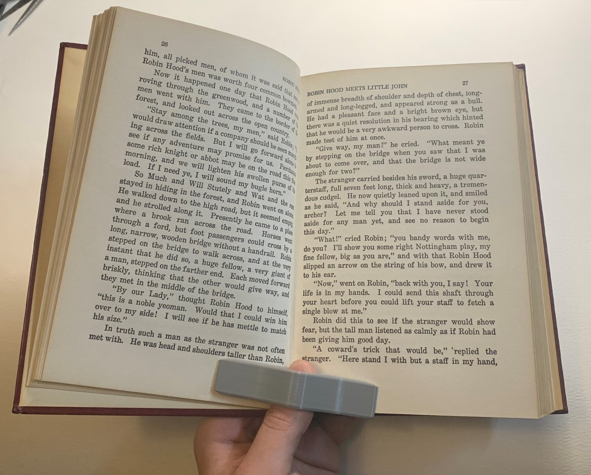 Person using book holder device to hold open pages of a book with one hand.