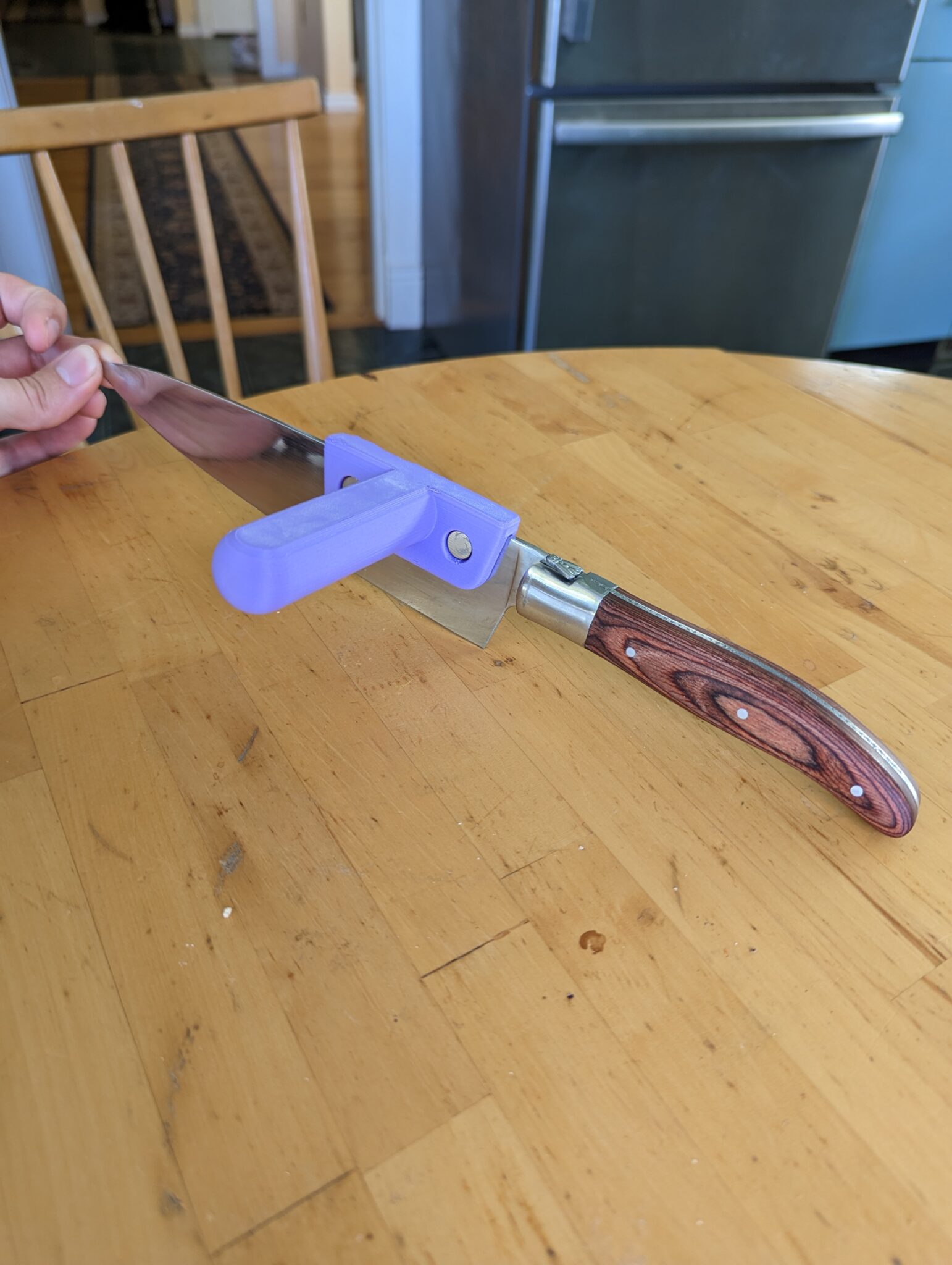 Hand holding a large kitchen knife with the knife aid installed.