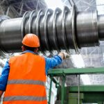 An engineer wearing a high visibility vest overlooks a giant pipe being fitted on a construction site.