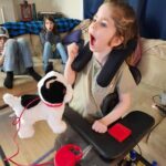 Briar in her wheelchair with her new switch-adapted toy and switch on a tray.