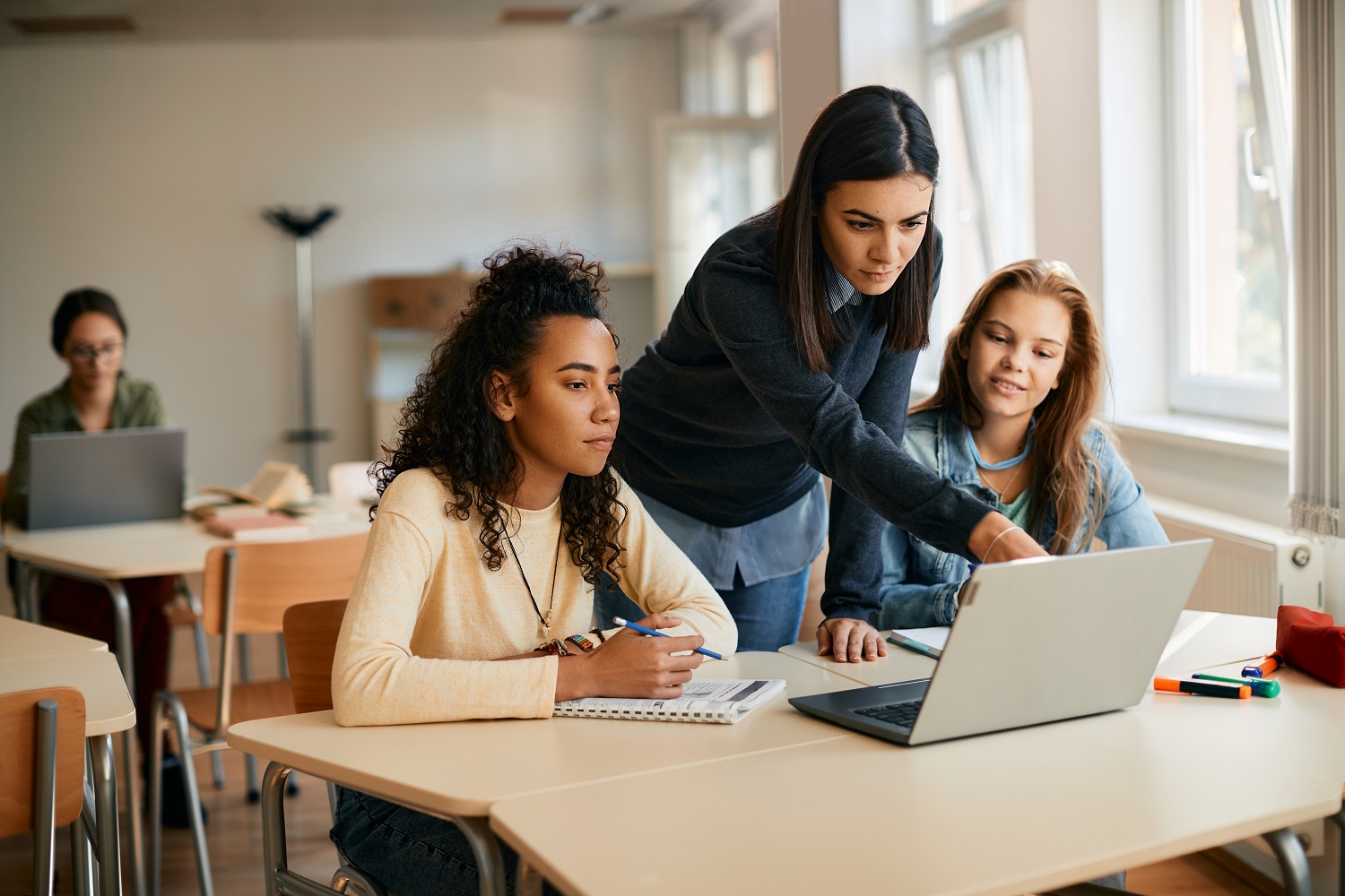 A high school professor assisting her students in e-learning on a laptop in the classroom.