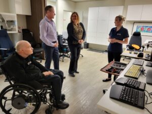 Gary Birch, Wayne Ackerman, and Elsa Chu Del Aguila talk in the Solutions lab in front of assistive technology.