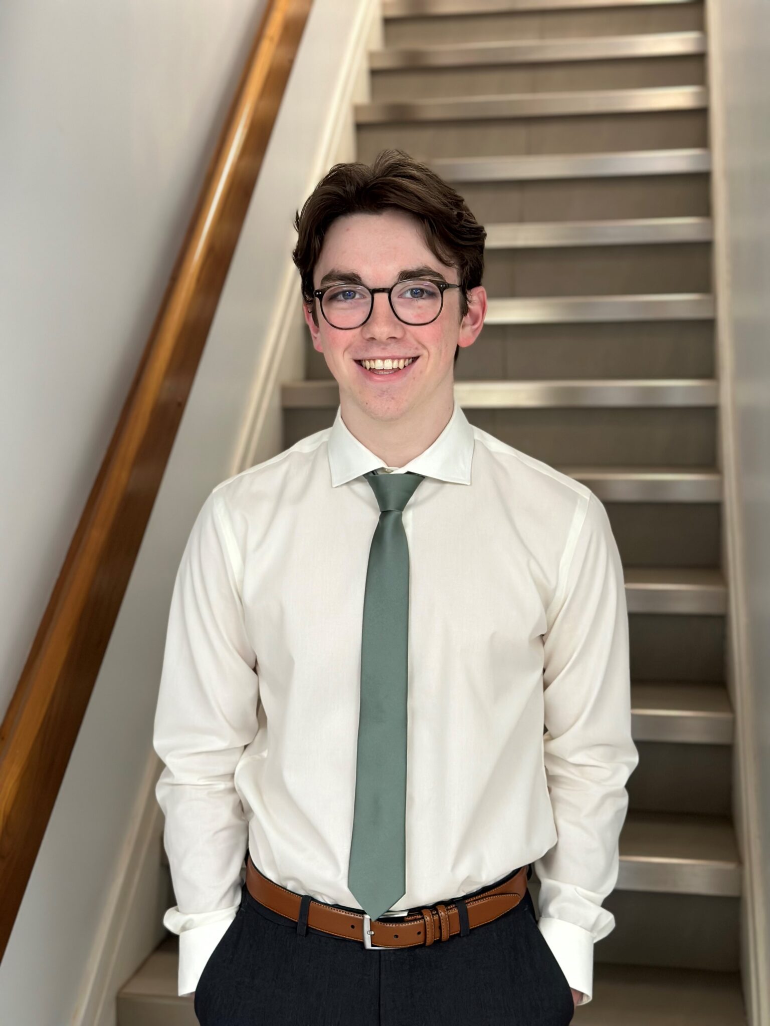 Isaac wearing a white shirt and a tie in front of a staircase