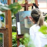 A woman paints on a canvas in a garden.