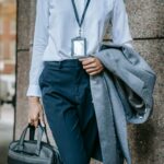 A woman holds her coat and briefcase in front of a building.