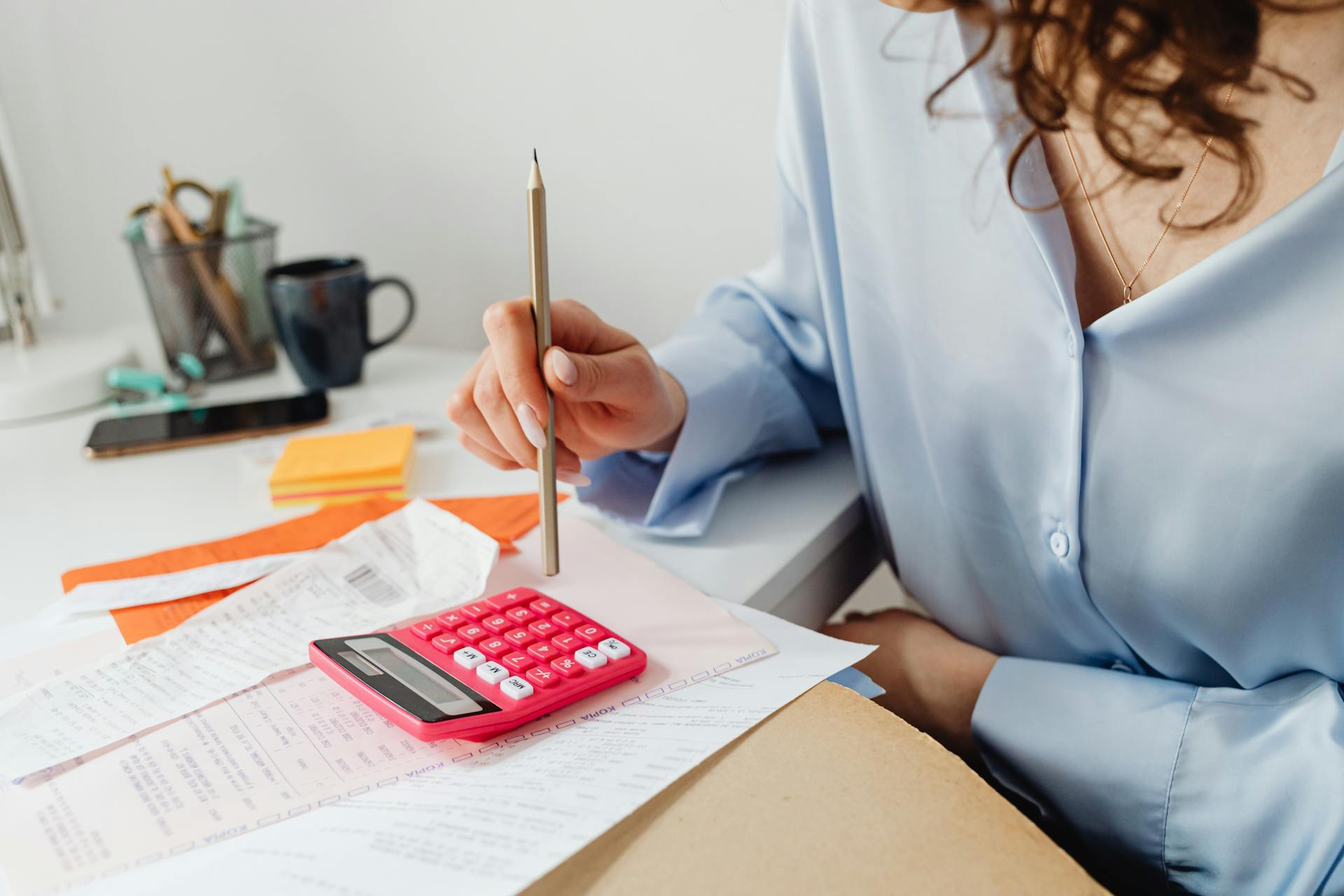 A woman looks over bills and uses a pencil to type on a calculator.