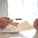 A man in a suit holding a pen and paper talks to a client.