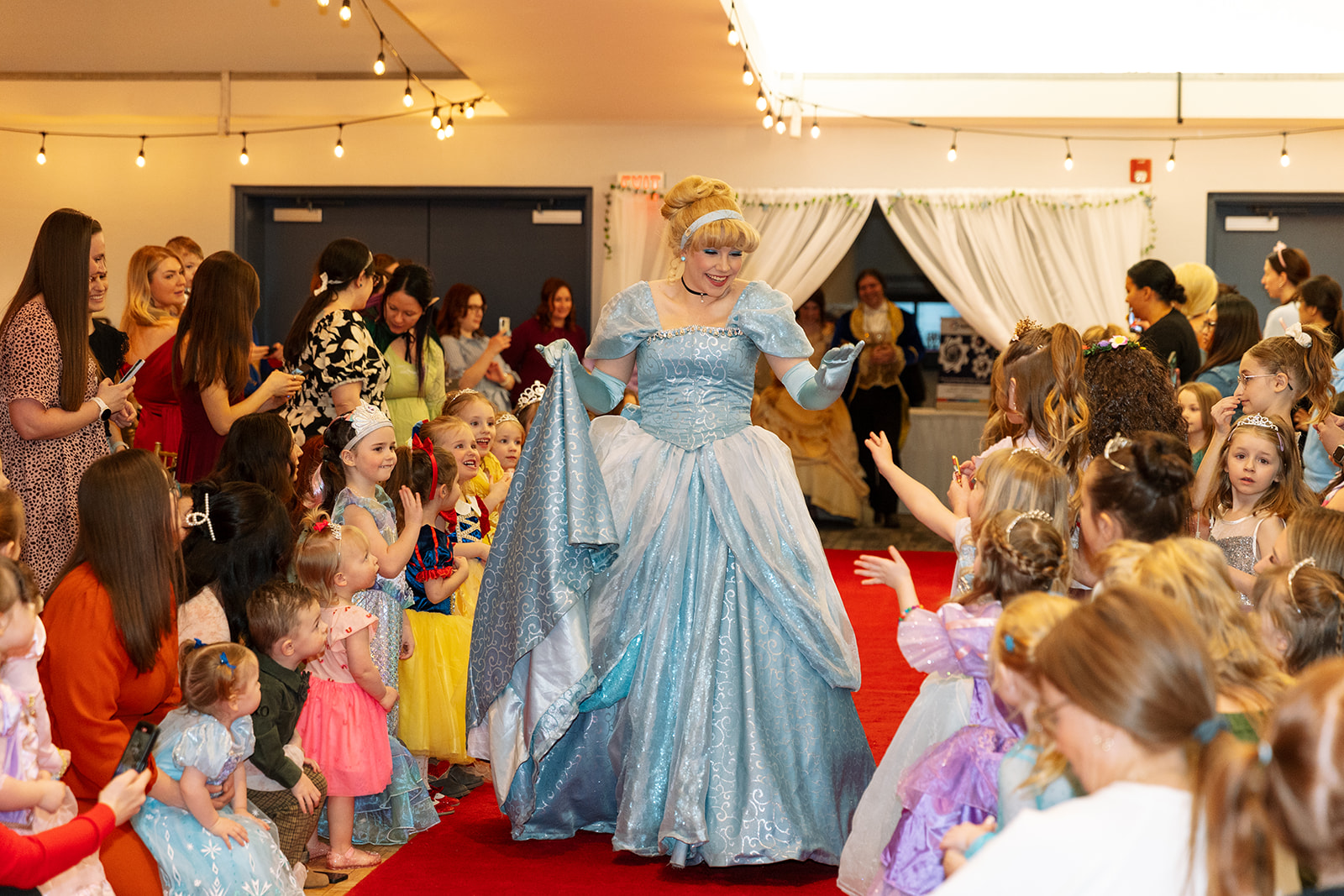 A performer dressed as Cinderella walks down the red carpet and waves to children in attendance.