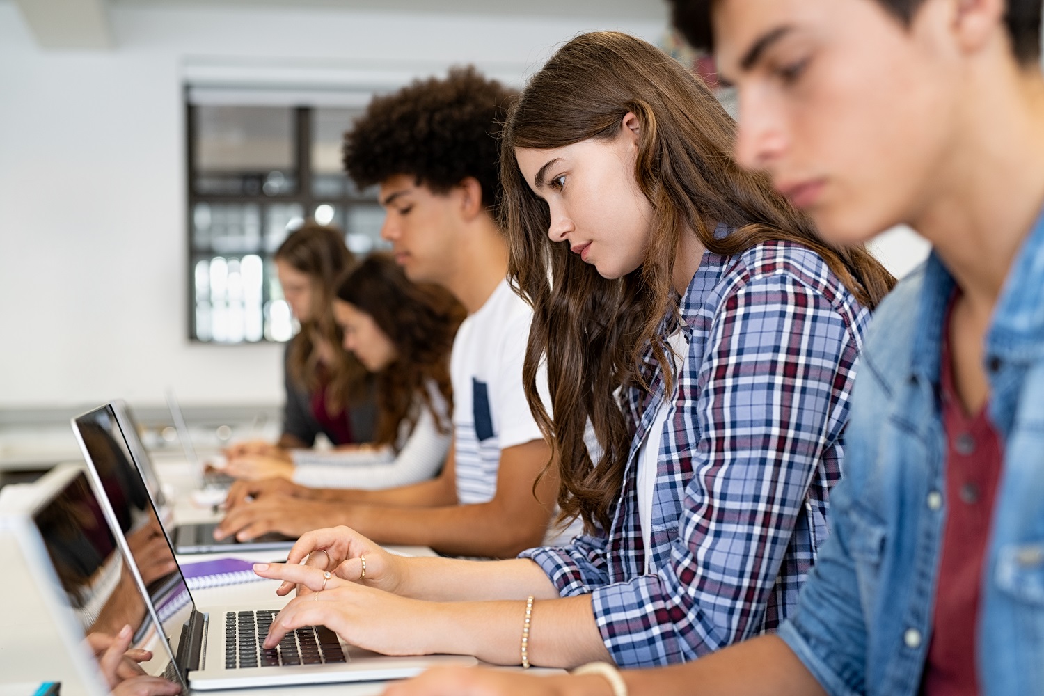 A female student uses her laptop next to other students also using laptops.