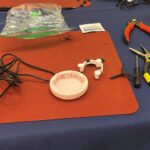 A soldering workstation with a 3D printed part, a cable, plyers, and various tools.