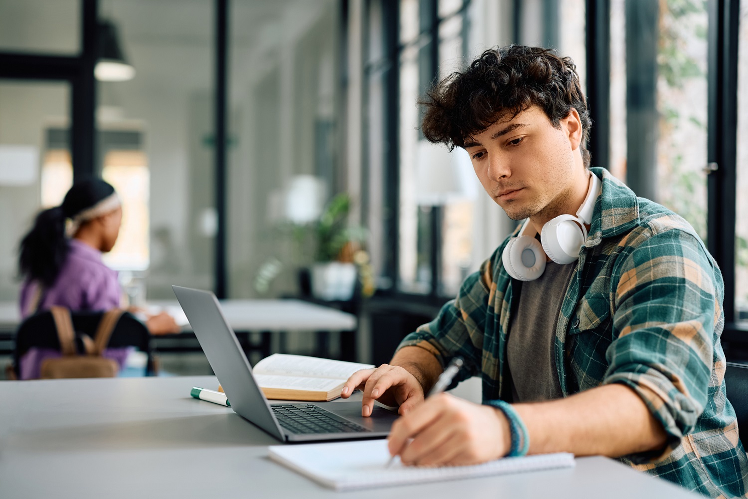 A student takes notes while going on a laptop.