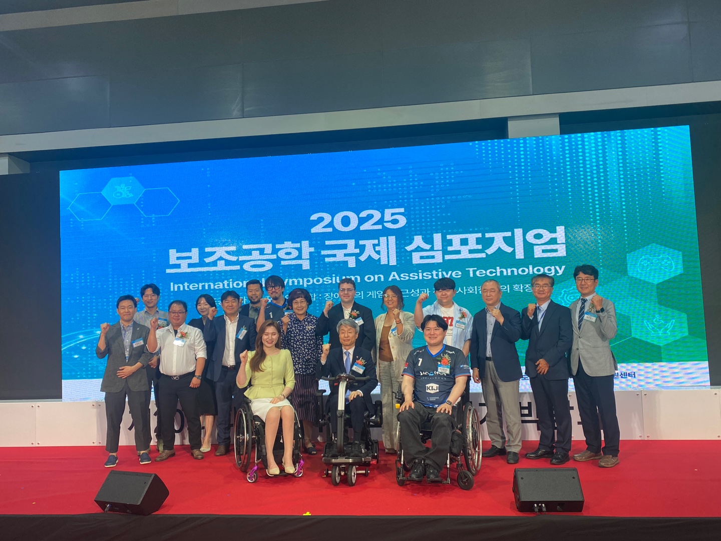 Tyler on stage for a large group photo with all the other presenters at the International Symposium on Assistive Technology.