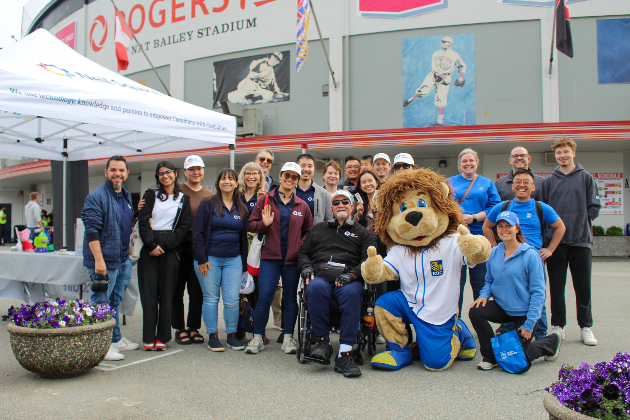 Neil Squire staff, RBC staff, and the RBC mascot Leo the Lion pose for a group photo outside Rogers Field at Nat Bailey Stadium.