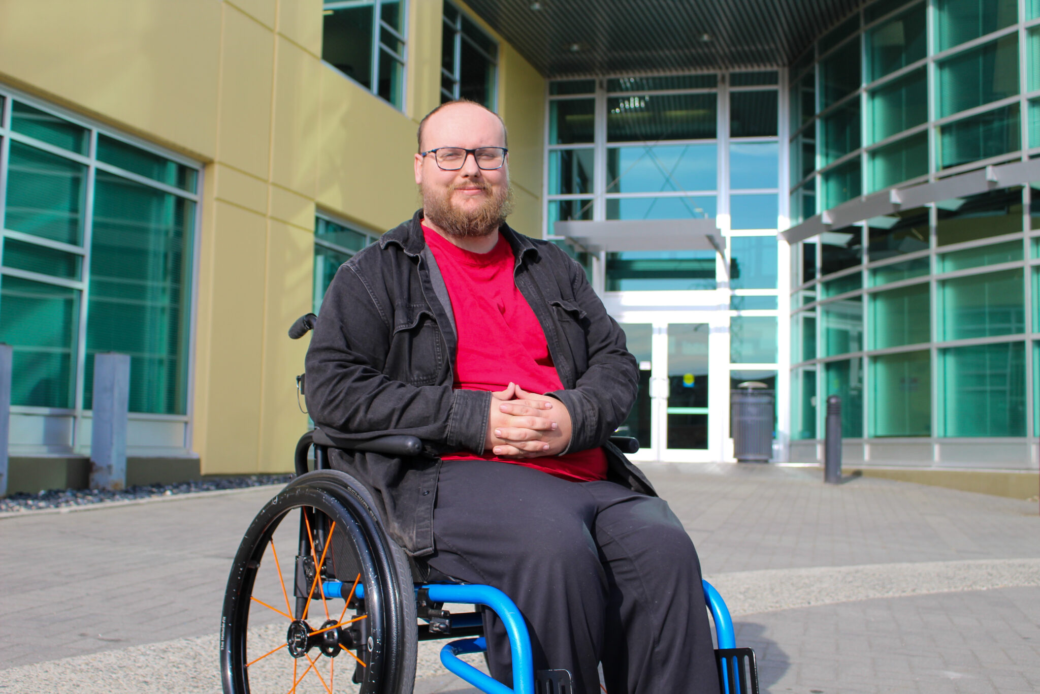 Thomas in a wheelchair in front of the exterior of Neil Squire's Burnaby office.