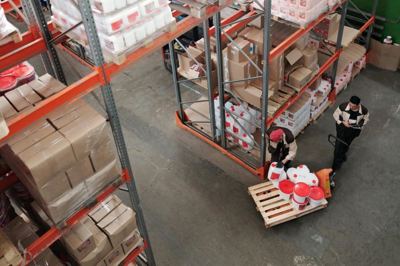 Workers in a warehouse loading a dolly with containers