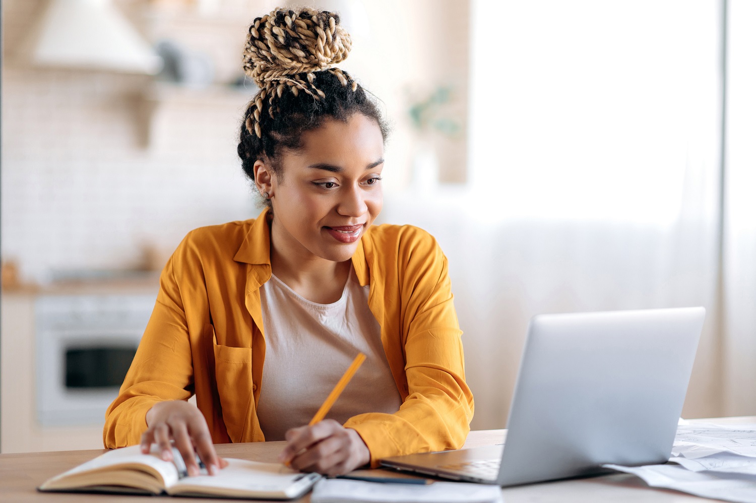 A woman writes into a notebook while using the laptop.
