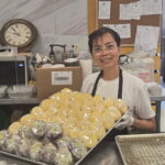 Maria holds a tray of baked goods at her workplace.