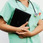 A nurse wearing scrubs and a stethoscope carries a file.