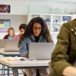 A woman in a classroom goes on laptop.