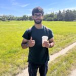Hamza standing in a field holding an iced coffee.