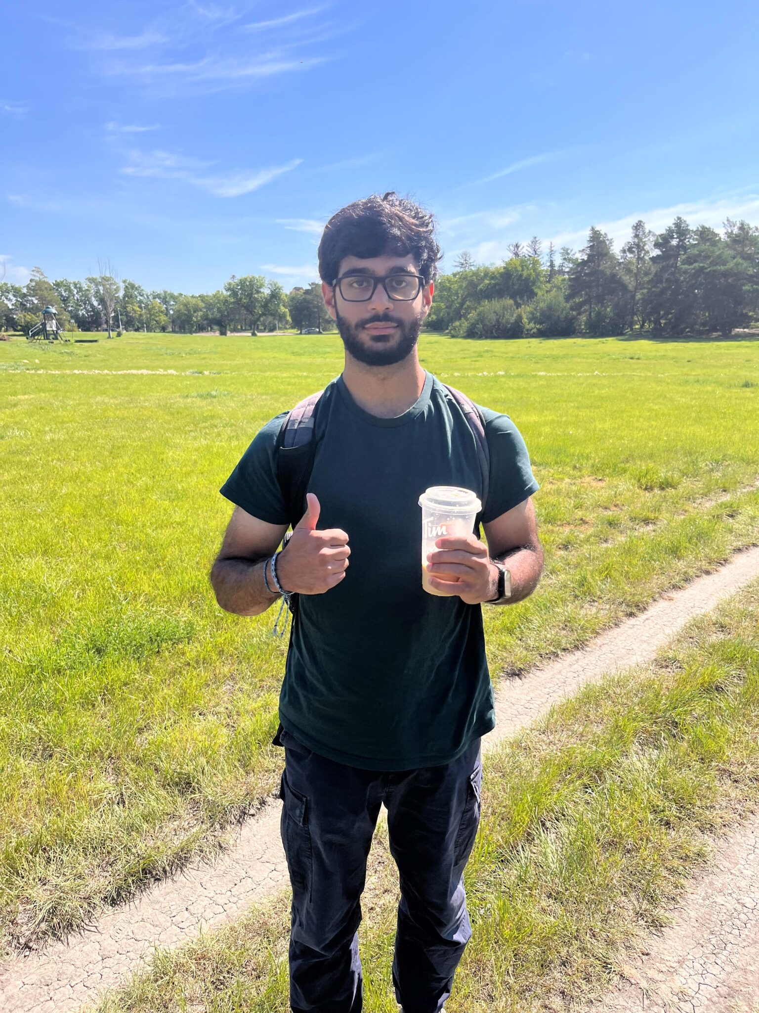 Hamza standing in a field holding an iced coffee.