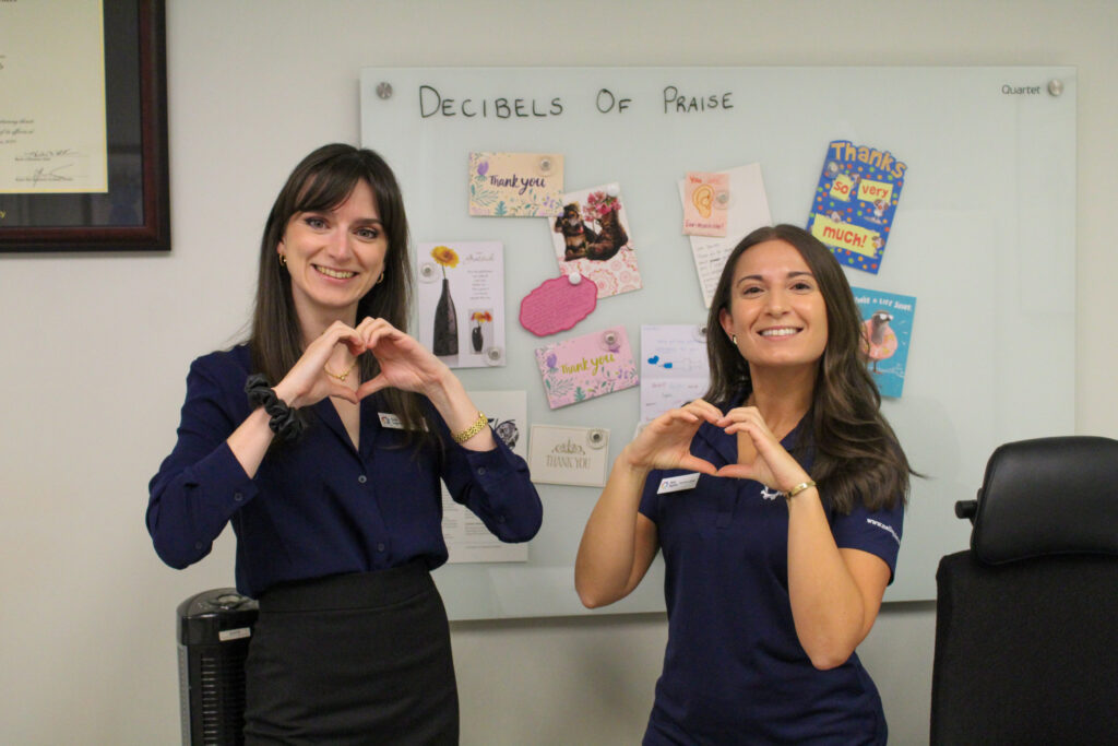 Heather and Danielle in front of the "decibels of praise" wall in their office.
